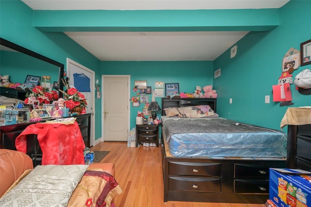 bedroom featuring beam ceiling, visible vents, and wood finished floors