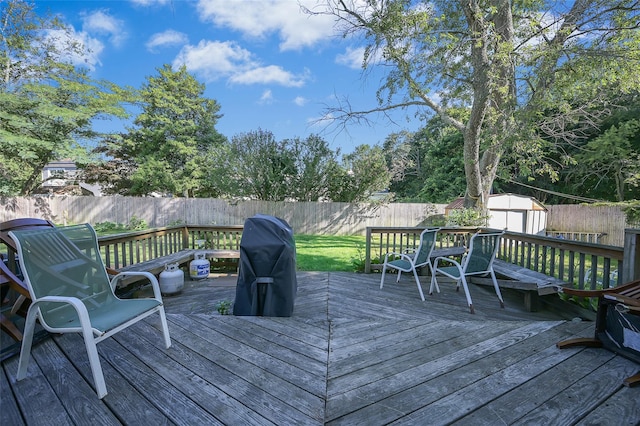 wooden deck featuring an outdoor structure, a shed, grilling area, and a fenced backyard
