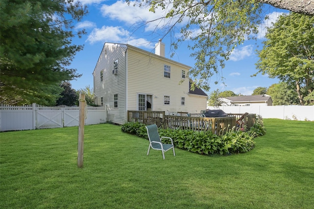 back of house featuring a chimney, a yard, a deck, and a fenced backyard