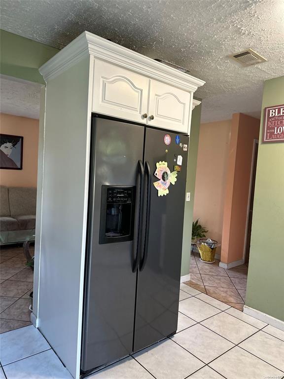 kitchen with a textured ceiling, black refrigerator with ice dispenser, visible vents, light tile patterned floors, and white cabinets