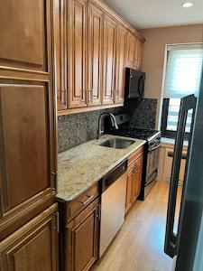 kitchen featuring light stone counters, light wood finished floors, a sink, decorative backsplash, and black appliances