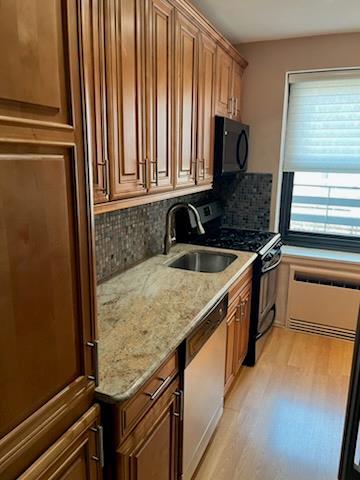kitchen with a sink, light wood-style flooring, decorative backsplash, and black appliances