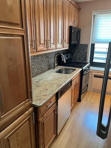 kitchen featuring a sink, black appliances, backsplash, light wood-style floors, and light stone counters