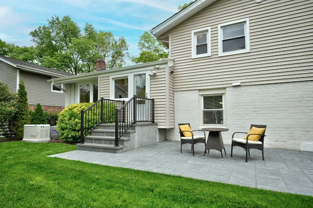 rear view of property with a chimney, a lawn, a patio, and brick siding
