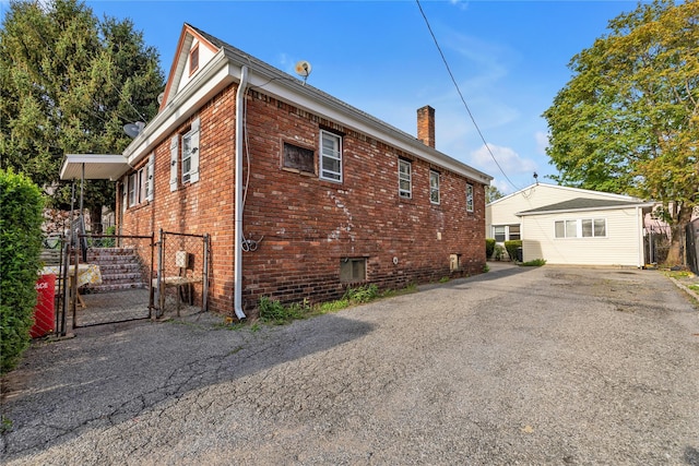 view of side of home with a gate, a chimney, fence, brick siding, and driveway