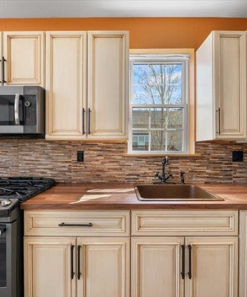 kitchen featuring butcher block countertops, a sink, stainless steel microwave, cream cabinets, and black gas range oven