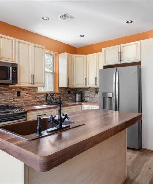 kitchen with stainless steel appliances, butcher block countertops, light wood-style floors, tasteful backsplash, and recessed lighting