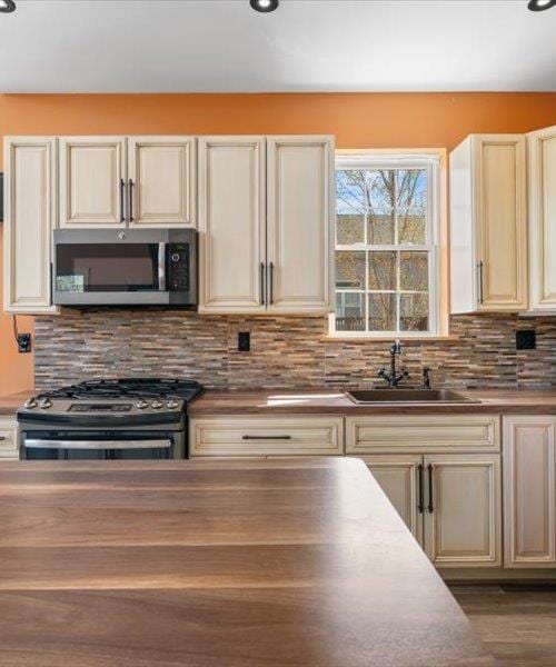 kitchen with stainless steel appliances, a sink, cream cabinetry, and tasteful backsplash