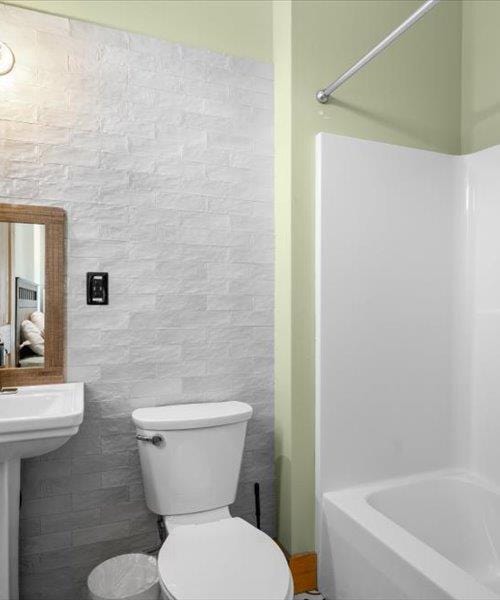 bathroom featuring toilet, tile walls, and washtub / shower combination