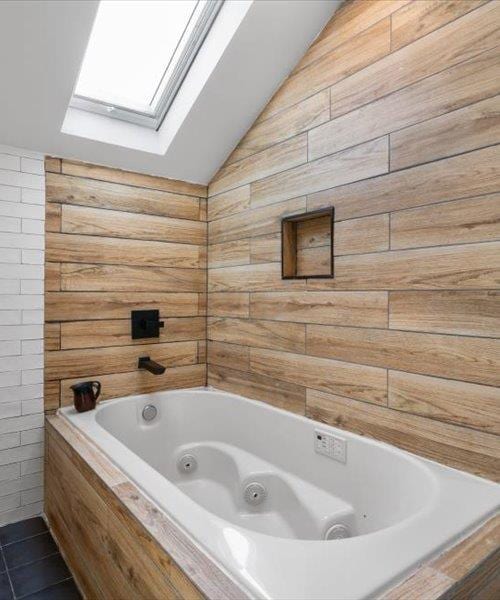 full bathroom featuring a skylight, lofted ceiling, a jetted tub, and tile patterned flooring