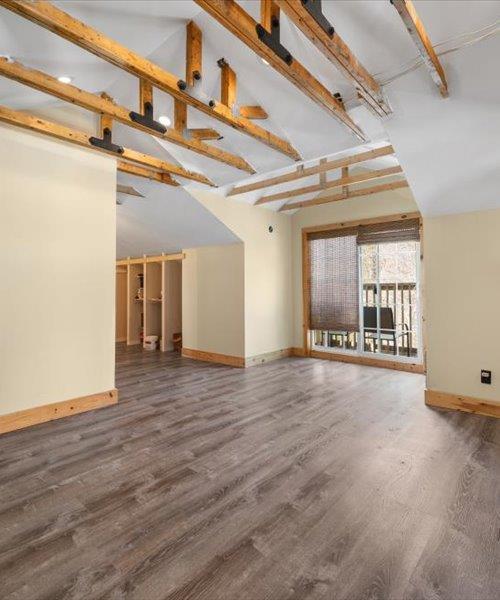 unfurnished living room featuring baseboards, wood finished floors, high vaulted ceiling, and beamed ceiling