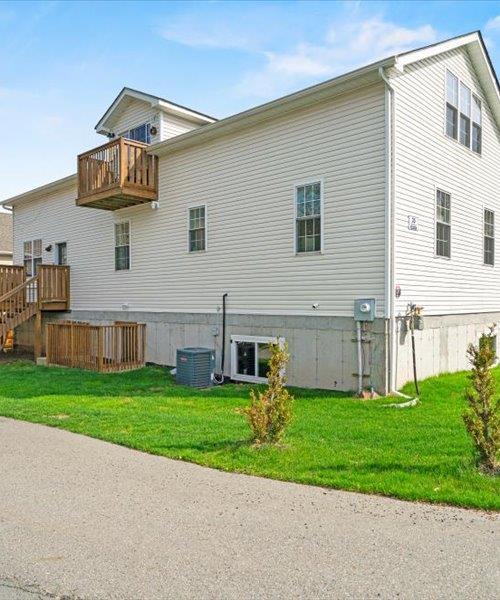 rear view of house with a balcony, a yard, and central AC unit