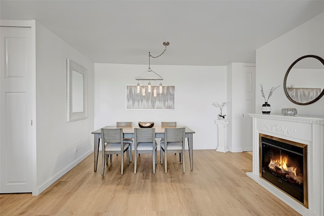 dining space featuring baseboards, a glass covered fireplace, and light wood-style floors