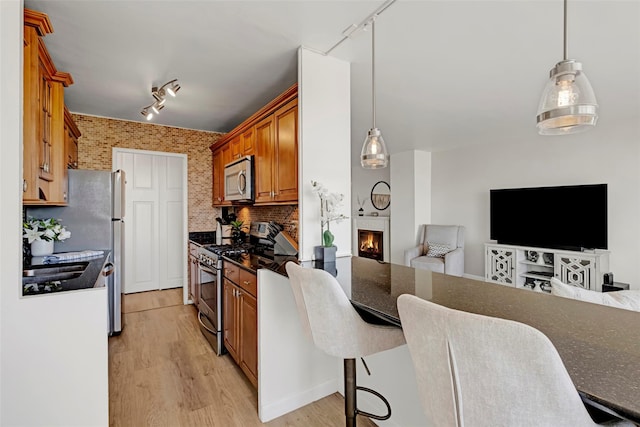 kitchen with rail lighting, stainless steel appliances, a warm lit fireplace, and open floor plan