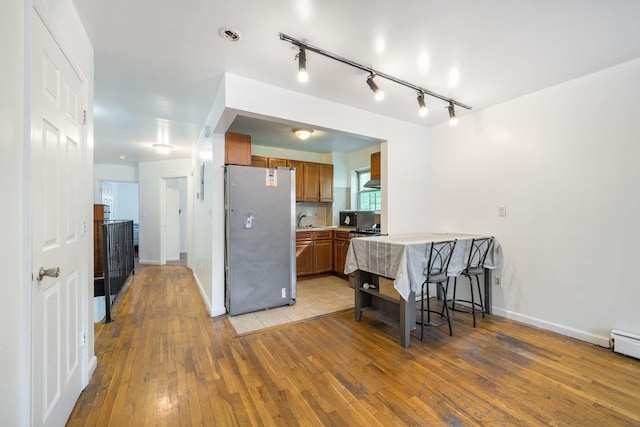 kitchen with a sink, brown cabinetry, freestanding refrigerator, light countertops, and light wood-style floors