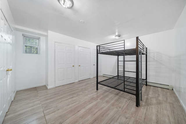 unfurnished bedroom with baseboards, light wood finished floors, baseboard heating, and a baseboard heating unit