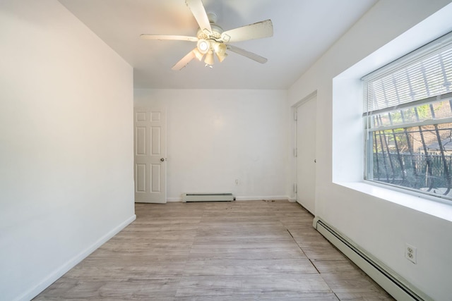 spare room featuring a baseboard heating unit, baseboards, light wood-type flooring, and a ceiling fan