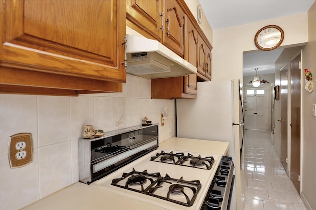 kitchen featuring brown cabinets, light countertops, gas range gas stove, and under cabinet range hood