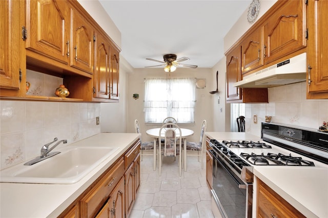 kitchen with brown cabinets, a sink, range with gas cooktop, under cabinet range hood, and light countertops
