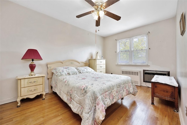 bedroom with light wood-type flooring, a ceiling fan, a wall mounted AC, and radiator heating unit
