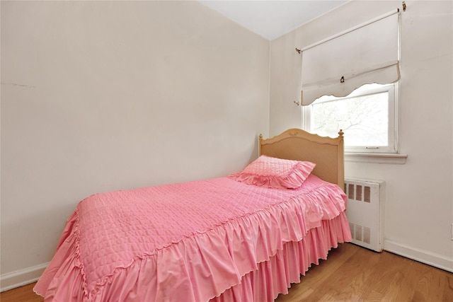 bedroom with wood finished floors, baseboards, and radiator heating unit