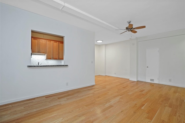 empty room with light wood finished floors, a ceiling fan, and baseboards