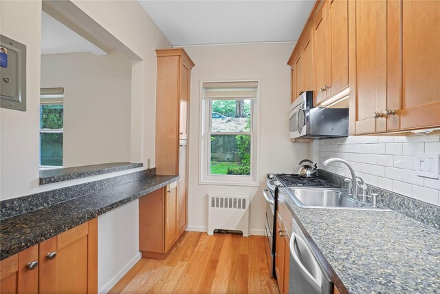 kitchen featuring radiator heating unit, appliances with stainless steel finishes, light wood-style flooring, a sink, and tasteful backsplash