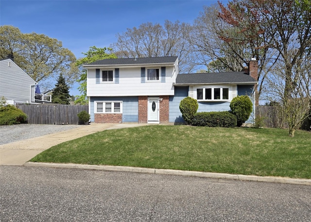tri-level home with fence, a chimney, brick siding, and a front yard