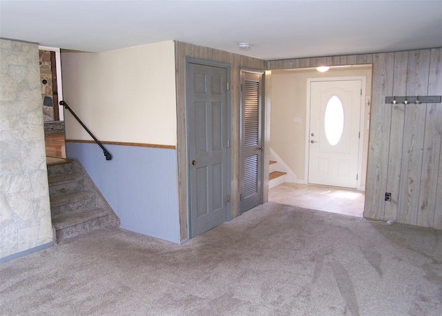 entrance foyer featuring stairs, carpet flooring, baseboards, and wooden walls