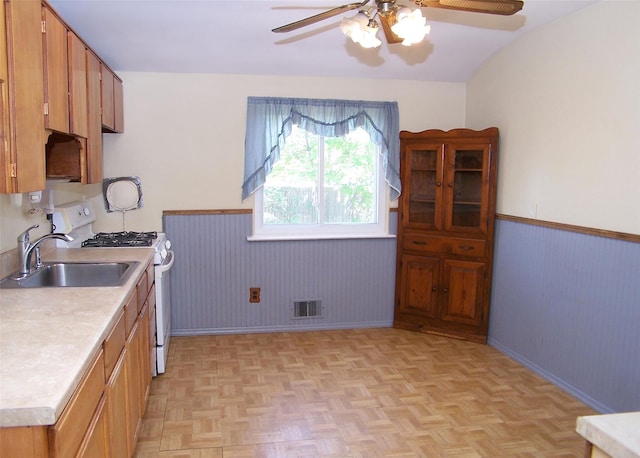 kitchen with white range with gas stovetop, a ceiling fan, a wainscoted wall, visible vents, and light countertops