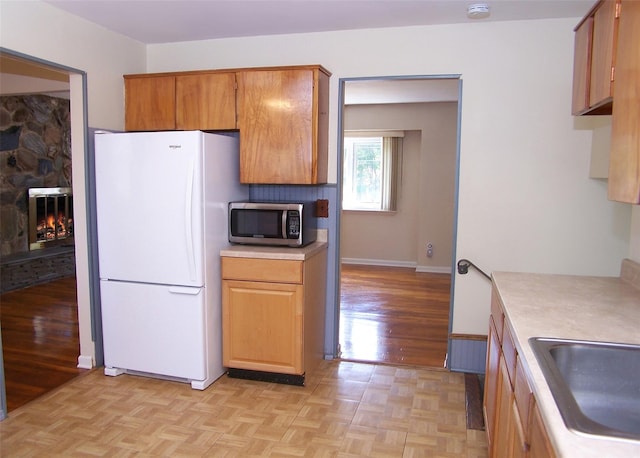 kitchen with stainless steel microwave, a sink, freestanding refrigerator, a fireplace, and light countertops