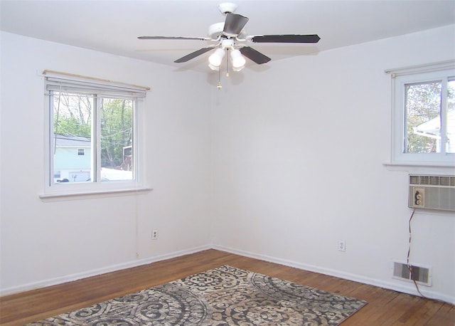 spare room with wood finished floors, visible vents, a ceiling fan, a wall unit AC, and baseboards