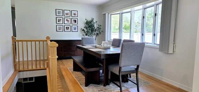 dining room featuring baseboards, a healthy amount of sunlight, ornamental molding, and light wood finished floors