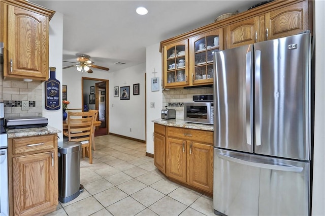 kitchen featuring tasteful backsplash, brown cabinets, freestanding refrigerator, ceiling fan, and light tile patterned floors