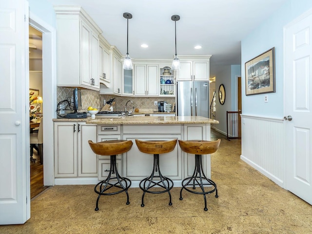 kitchen featuring a peninsula, glass insert cabinets, freestanding refrigerator, backsplash, and decorative light fixtures