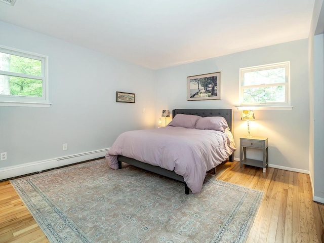 bedroom with a baseboard heating unit, baseboards, hardwood / wood-style floors, and multiple windows