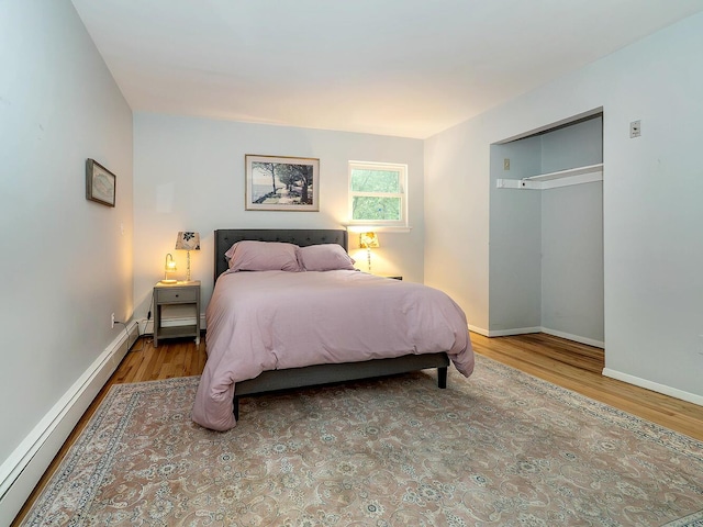 bedroom with a baseboard heating unit, baseboards, and wood finished floors