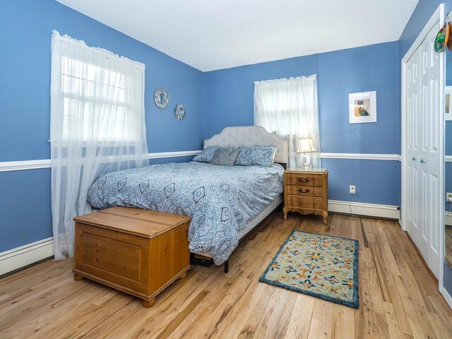 bedroom with multiple windows, a closet, wood finished floors, and a baseboard heating unit