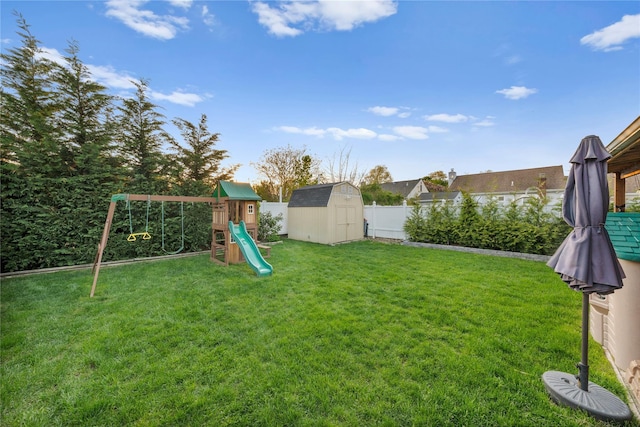 view of yard featuring a storage unit, a playground, a fenced backyard, and an outbuilding