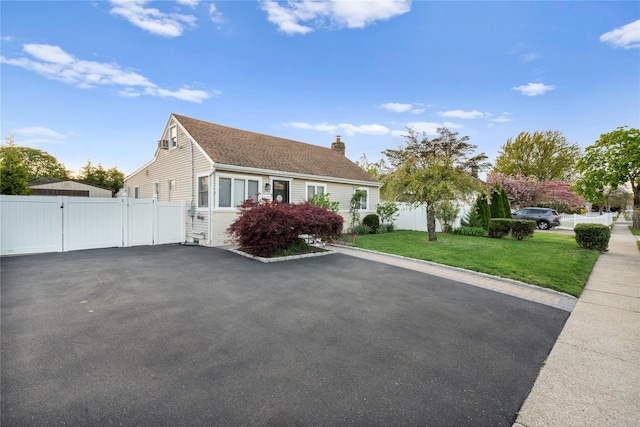 view of front of house featuring a gate, fence, driveway, a front lawn, and a chimney
