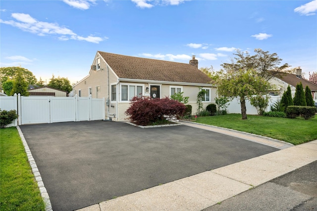 cape cod home featuring a gate, fence, a chimney, a front yard, and driveway