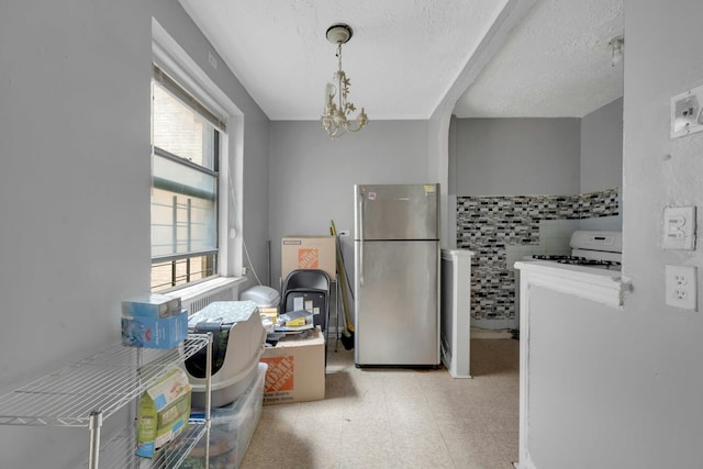 kitchen featuring freestanding refrigerator, light flooring, a textured ceiling, a chandelier, and white gas range