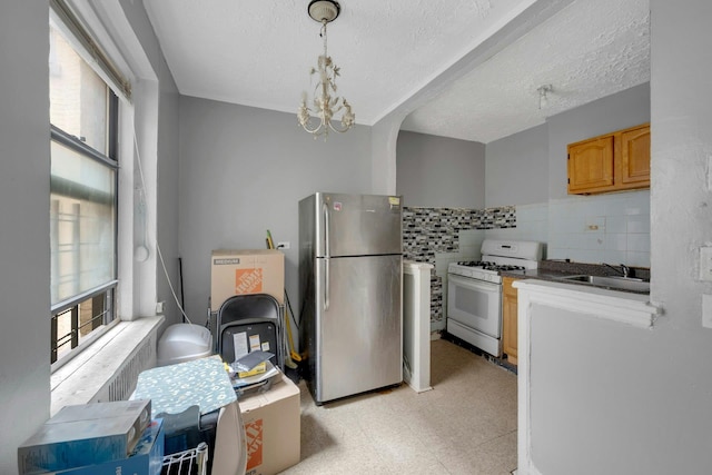 kitchen with freestanding refrigerator, white gas range oven, light flooring, a sink, and a chandelier
