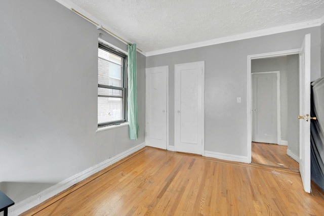 unfurnished bedroom featuring a textured ceiling, light wood-style floors, baseboards, and ornamental molding