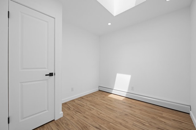 spare room featuring a skylight, recessed lighting, a baseboard radiator, light wood finished floors, and baseboards