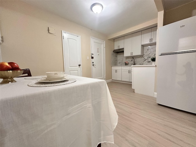 bedroom featuring a sink, freestanding refrigerator, baseboards, and light wood finished floors