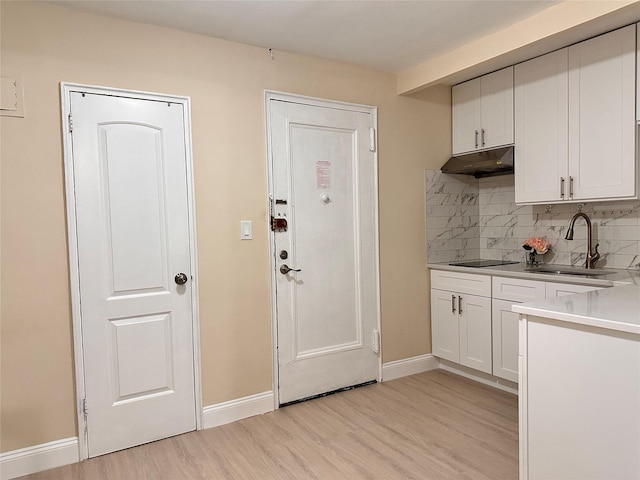 kitchen with under cabinet range hood, a sink, black electric cooktop, tasteful backsplash, and light wood-type flooring