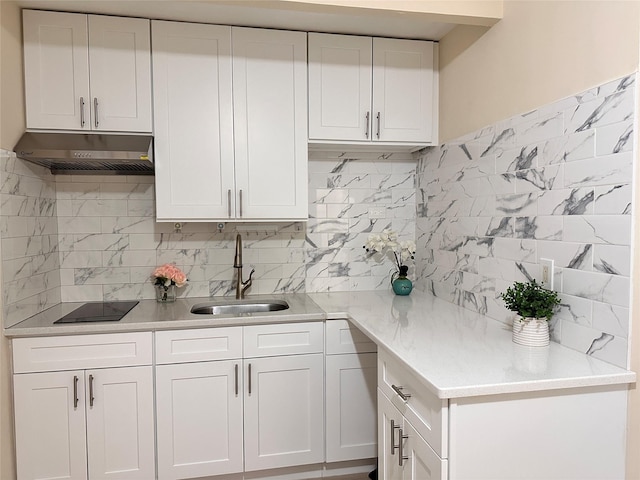 kitchen featuring under cabinet range hood, a sink, white cabinetry, backsplash, and black electric stovetop