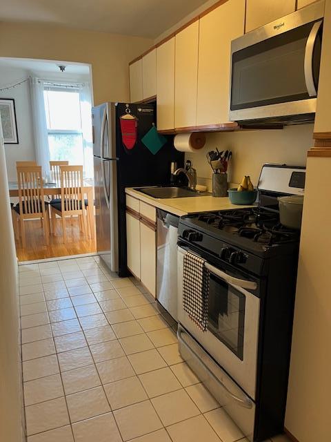 kitchen featuring a sink, stainless steel appliances, white cabinetry, light countertops, and light tile patterned floors