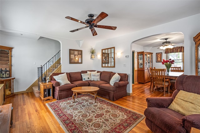 living room with stairs, ceiling fan, arched walkways, baseboards, and light wood-style floors